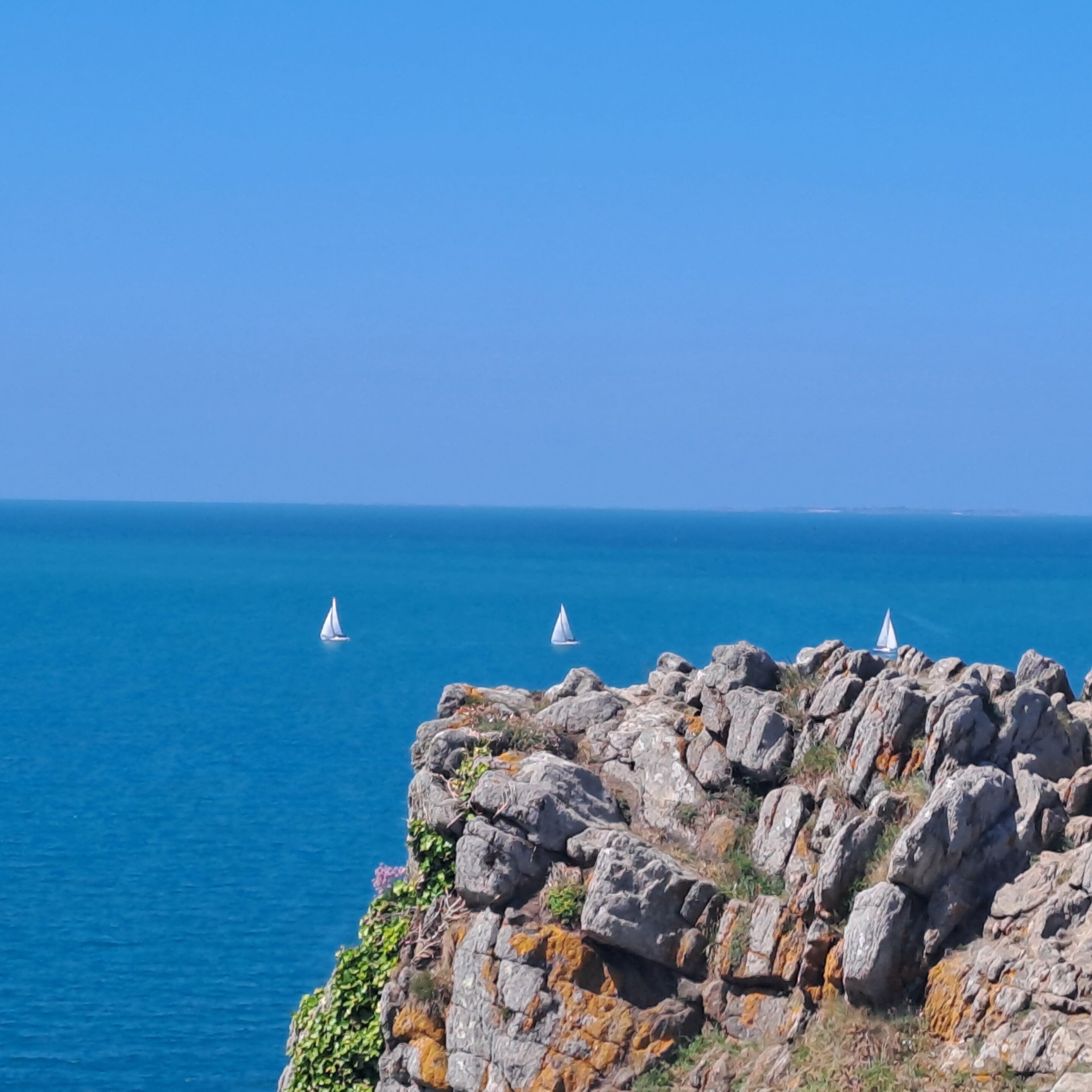 A rocky coastline with clear blue sea and sailboats.