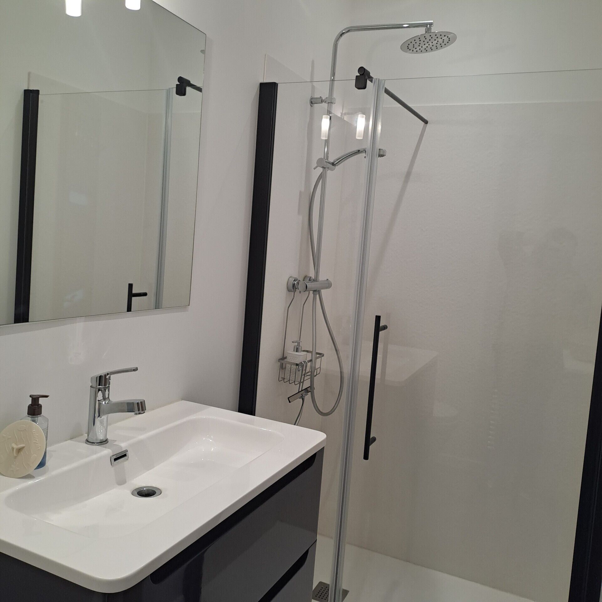 Une salle de bain moderne avec un lavabo blanc, un miroir et une douche.