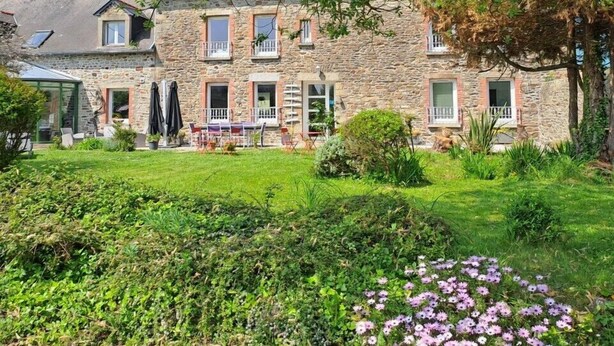 Een stenen gebouw met een tuin ervoor, met een terras met stoelen en een tafel.