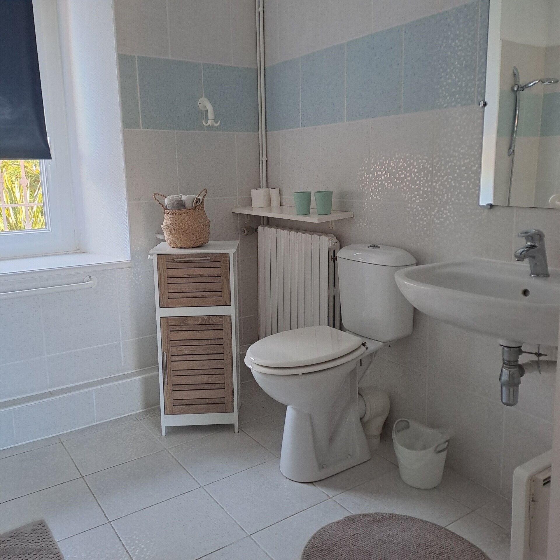 Une salle de bain équipée de toilettes, d’un lavabo et d’une fenêtre donnant sur un espace verdoyant.