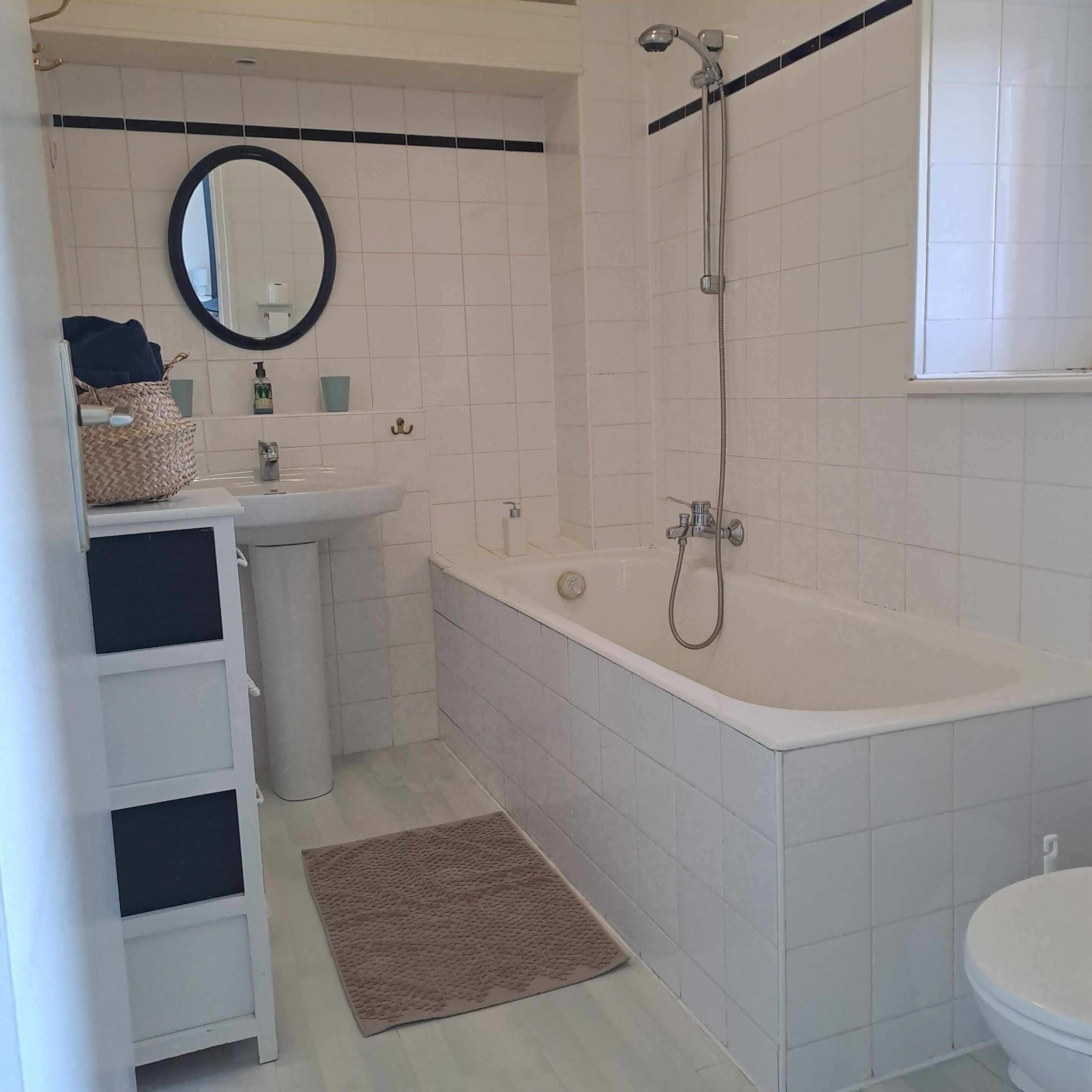 Un bagno con lavandino bianco, specchio e vasca da bagno. Si notano un porta asciugamani e un piccolo tappeto sul pavimento.