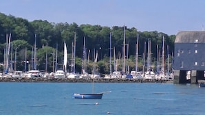 Een jachthaven met verschillende zeilboten afgemeerd, een klein blauw bootje op de voorgrond en een gebouw op palen aan de rechterkant.