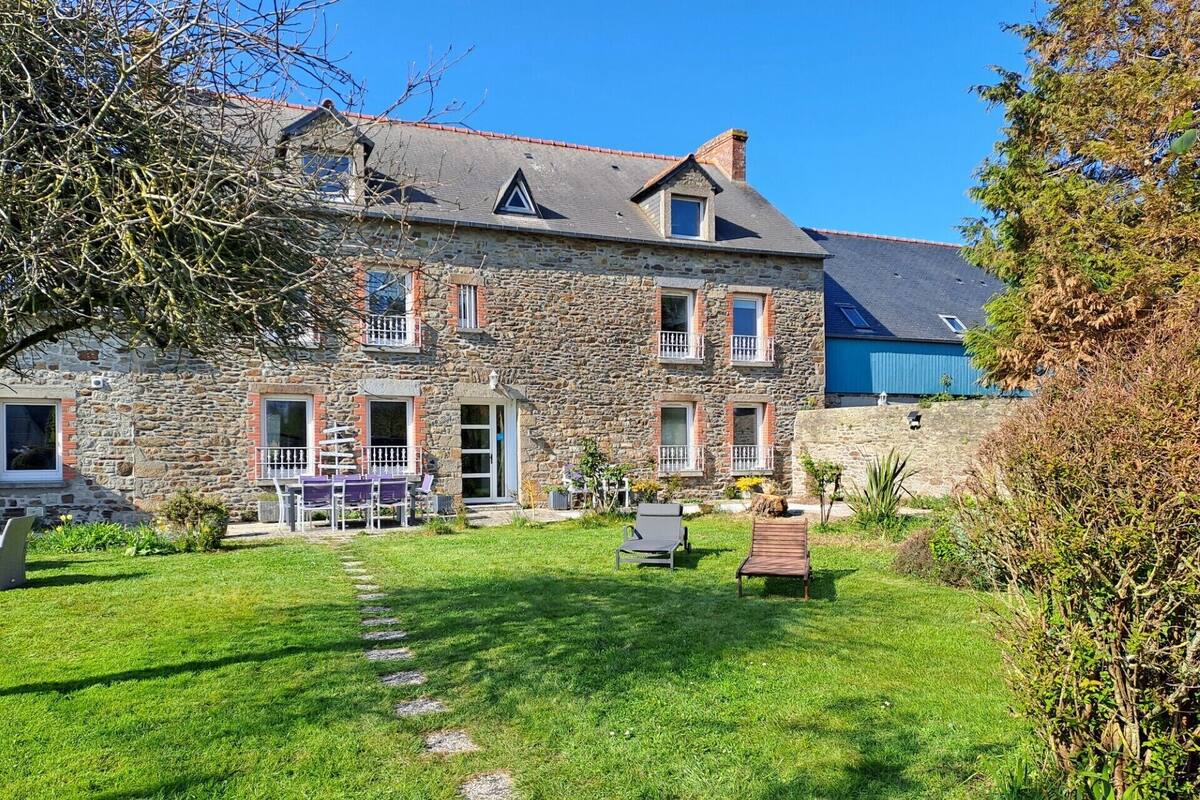 Une maison en pierre avec une pelouse bien entretenue et un espace extérieur aménagé pour s’asseoir.