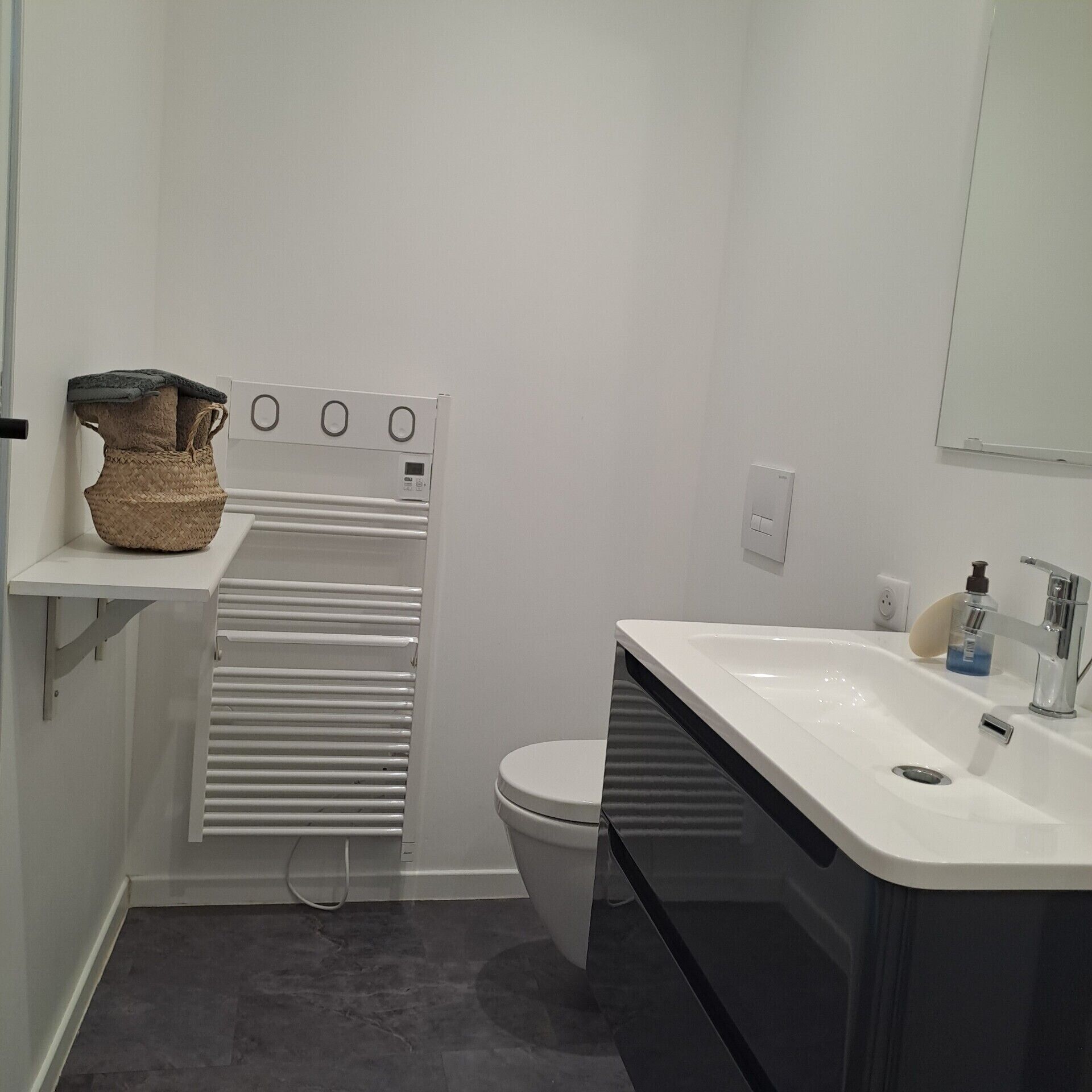 A modern bathroom with a white sink, a toilet, and a built-in heater.