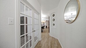 Un couloir avec une porte blanche, un miroir et un luminaire fixé au mur.
