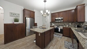 Une cuisine moderne avec des meubles de couleur bois foncé, des plans de travail en granit, des appareils électroménagers en acier inoxydable et un îlot central.