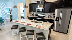Una cocina moderna con armarios oscuros, electrodomésticos de acero inoxidable, encimera de granito y taburetes de bar.
