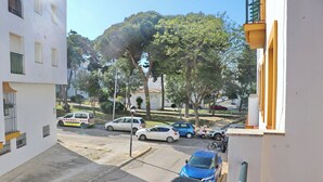 Vista de la calle con autos estacionados, un vehículo de emergencia amarillo y un edificio con balcones.