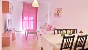 Una sala acogedora con un sofá, una mesa de comedor con sillas, un televisor y una cortina rosa.