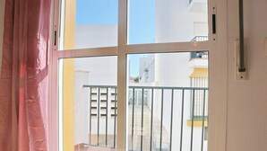 Un balcón con barandilla de metal, piso de baldosas y vista a un edificio blanco con balcones.