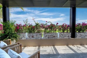 A covered outdoor seating area with wicker furniture and planters of pink flowers.