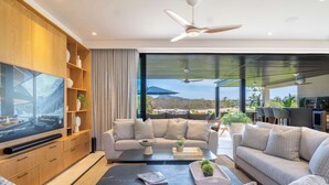 A modern living room with a large flat-screen TV, a sofa, a coffee table, and a dining area with chairs and a table. - Porta Fortuna (Punta de Mita)