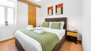 Ein ordentlich eingerichtetes Schlafzimmer mit Bett, Nachttischen, einem Fenster mit Pflanze und einer Holztür.