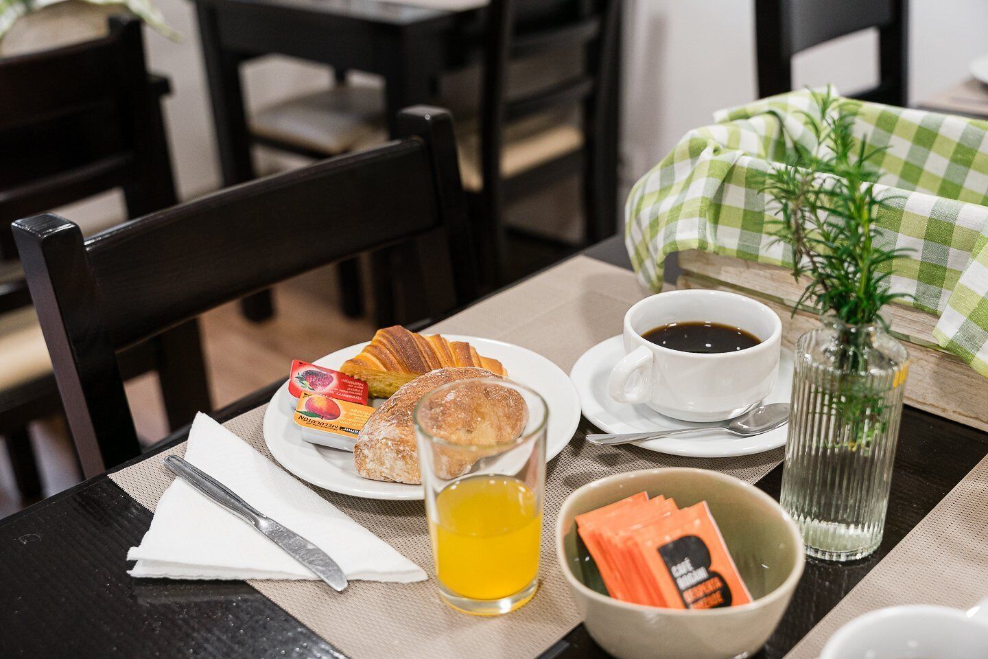 A table set with a croissant, a pastry, a cup of coffee, a glass of juice, and a bowl of snacks.