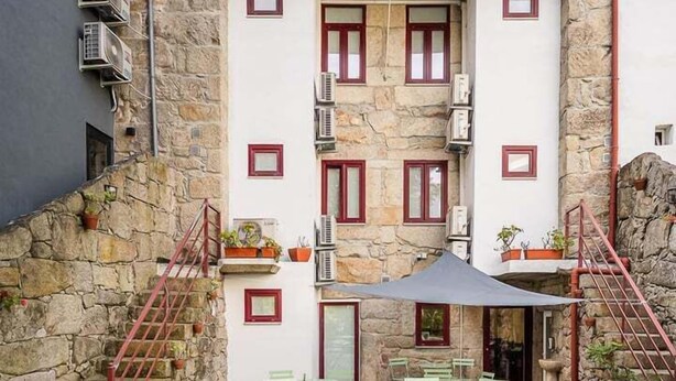 Un edificio de fachada de piedra, con varias ventanas y un patio con mobiliario exterior.