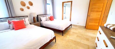 A hotel room with two beds, a wooden wardrobe, a mirror, and a window with curtains.