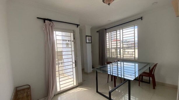 A spacious room with a glass dining table, two chairs, a ceiling fan, and large windows with curtains. - Combretrata (Phnom Penh)