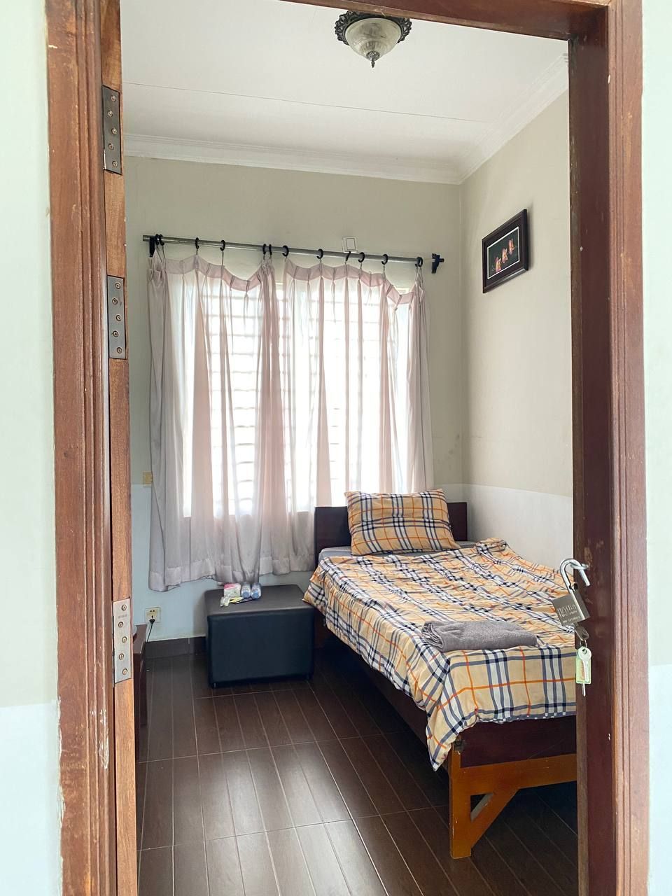 A small, cozy bedroom with a bed, a nightstand, and a window with sheer curtains.