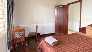 A hotel room with a bed, a wooden chair, a small table, and a door. - Combretrata (Phnom Penh)
