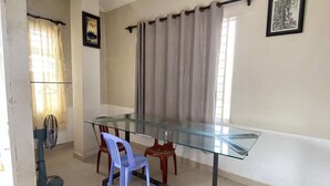 A dining area with a glass-top table, two chairs, a ceiling fan, and a window with curtains. - Combretrata (Phnom Penh)
