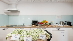 A modern kitchen with a white and light blue color scheme, equipped with a sink, coffee machines, and a fruit display. - GuestReady - Invicta Porto GuestHouse - Room 003 (Porto)