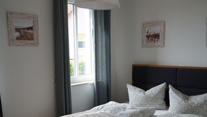 Et soveværelse med en seng, et vindue med gardiner, en hængende lampe og to billeder i rammer på væggen.