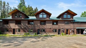 A large log cabin with a stone foundation, multiple windows, and a gravel driveway. - Lookout Lodge at Cavanaugh's (Coolin)