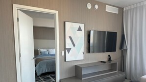 A modern hotel room with a bed, a TV mounted on the wall, a small seating area, and a door leading to another room. - 2201 (Hollywood)