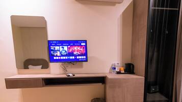 Habitación de hotel con televisor de pantalla plana montado sobre un escritorio de madera, un cesto de basura y un panel de vidrio.