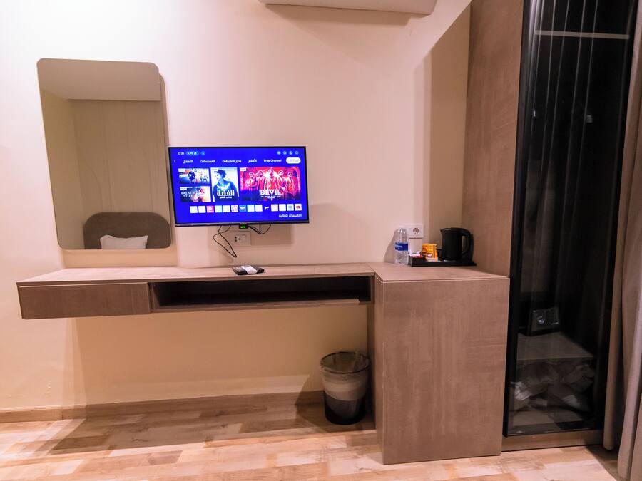 Habitación de hotel con televisor de pantalla plana montado sobre un escritorio de madera, un cesto de basura y un panel de vidrio.
