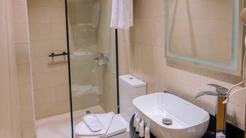 Un baño moderno con ducha de vidrio, lavamanos blanco y un espejo grande.