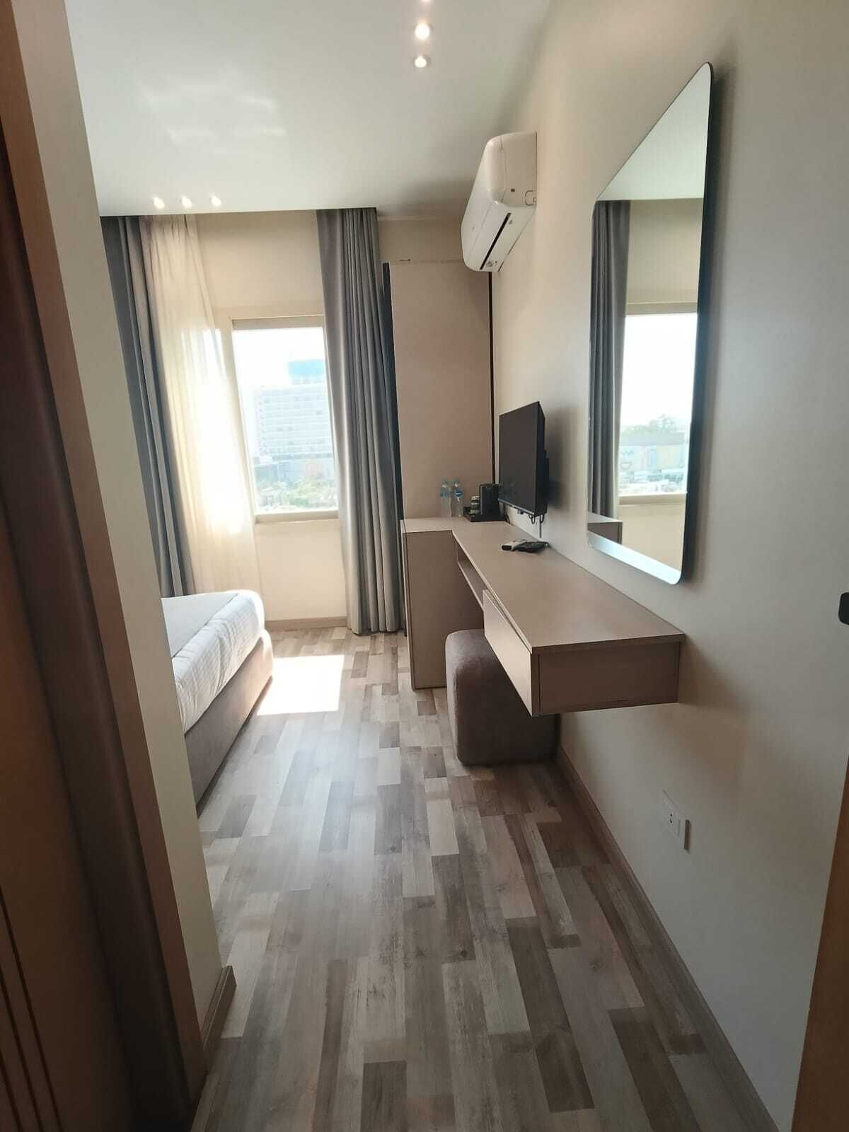 A hotel room with a bed, a desk, a chair, a TV, and a large window.