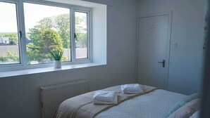 Een slaapkamer met een bed, een radiator, een raam met uitzicht en een deur.