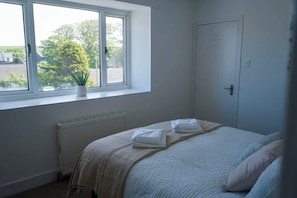 A bedroom with a bed, a radiator, a window with a view, and a door.