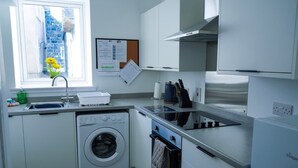Een kleine keuken met een wasmachine, een fornuis en een raam met uitzicht op een stenen gebouw.