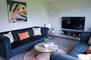 A living room with a black sofa, a round coffee table, a flat-screen TV, and a decorative painting on the wall.