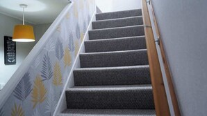 Una escalera con peldaños alfombrados, barandilla de madera y una lámpara colgante amarilla.