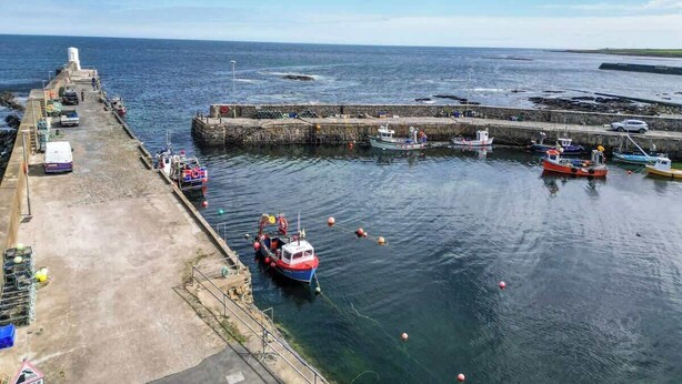 Un puerto con barcos amarrados, un muelle y un faro al fondo.