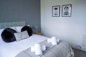 A neatly made bed with a pillow labeled 'Be Our Guest,' a bedside table with a lamp, and two framed pictures on the wall.