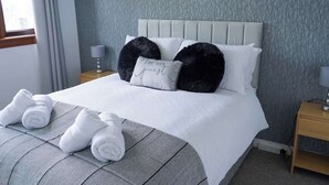 Una cama bien hecha con cabecera, una almohada con texto y toallas enrolladas sobre la cama.