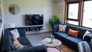 Una sala de estar con televisor, sofás, una mesa de centro y un ventanal grande.