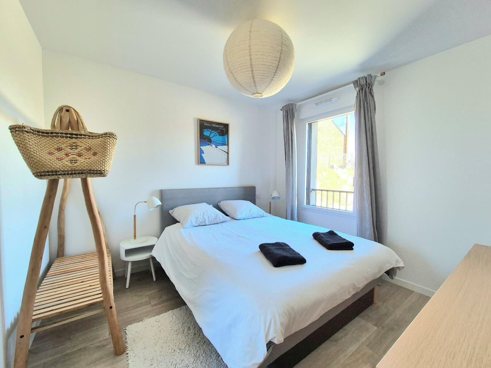 A bedroom with a bed, a standing lamp, a woven basket, and a framed picture on the wall.