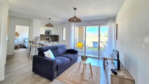 A modern apartment with a dark grey sofa, a small rug, and a dining area with a table and chairs. - Beautiful apartment with balcony and garden (Saint-Coulomb)