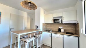 A compact kitchen with a wooden island, white bar stools, a microwave, a toaster, and a dishwasher. - Beautiful apartment with balcony and garden (Saint-Coulomb)