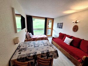 A room with a table, chairs, a red sofa, a window, and a balcony.