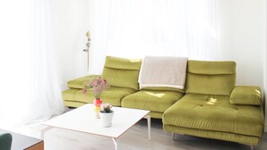 Ein Wohnzimmer mit einem grünen Sofa, einem weißen Couchtisch und einem Fenster mit leichtem Vorhang.
