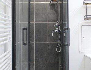 Une douche avec une porte en verre, un pommeau de douche à main et un flexible de douche.
