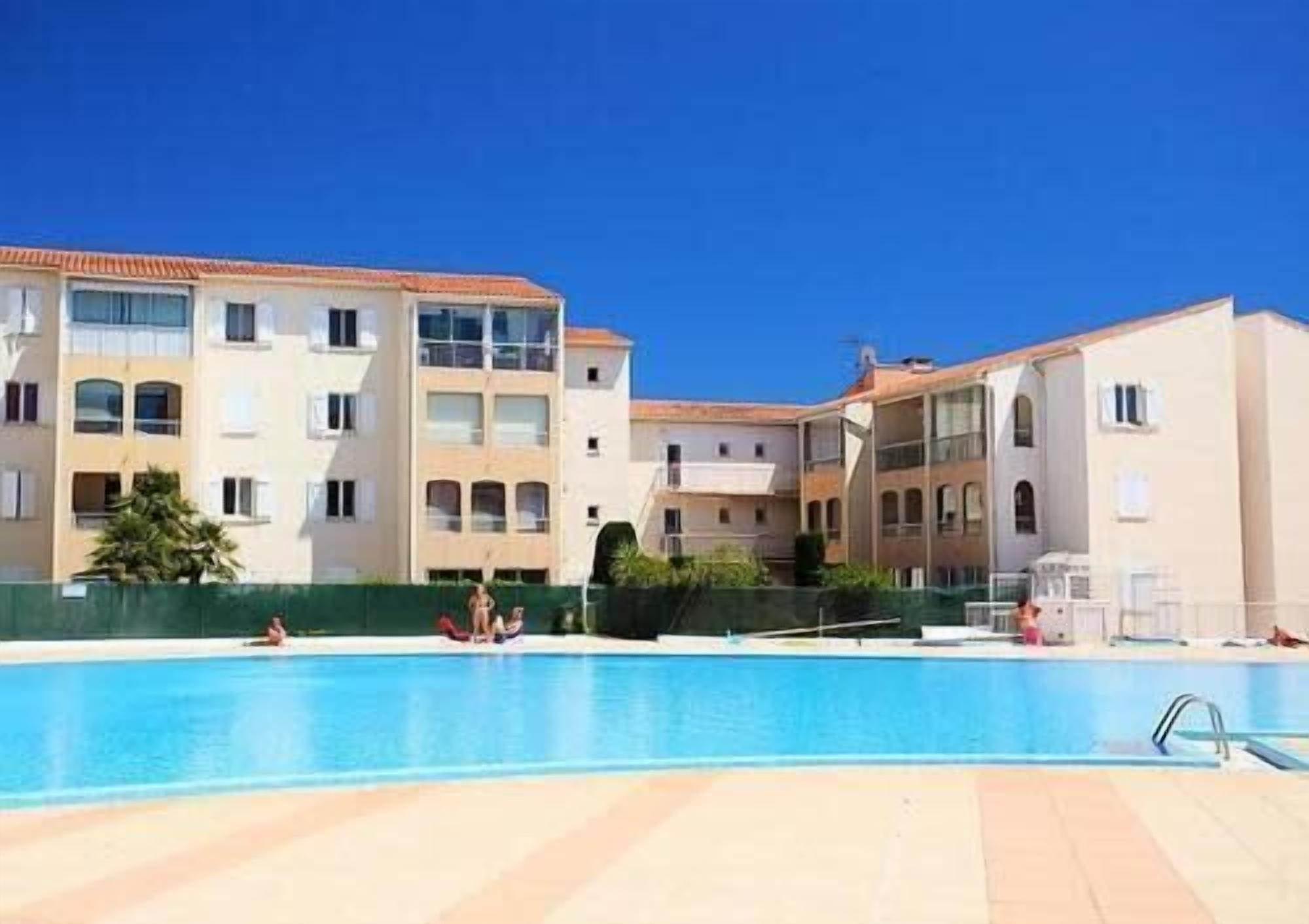 Zona de piscina con un cielo azul despejado, una piscina y un edificio con varios balcones y ventanas.