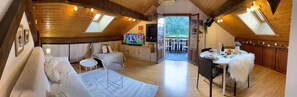 Een gezellig slaapkamer op zolder met een bank, een televisie en een eethoek met een tafel en stoelen.