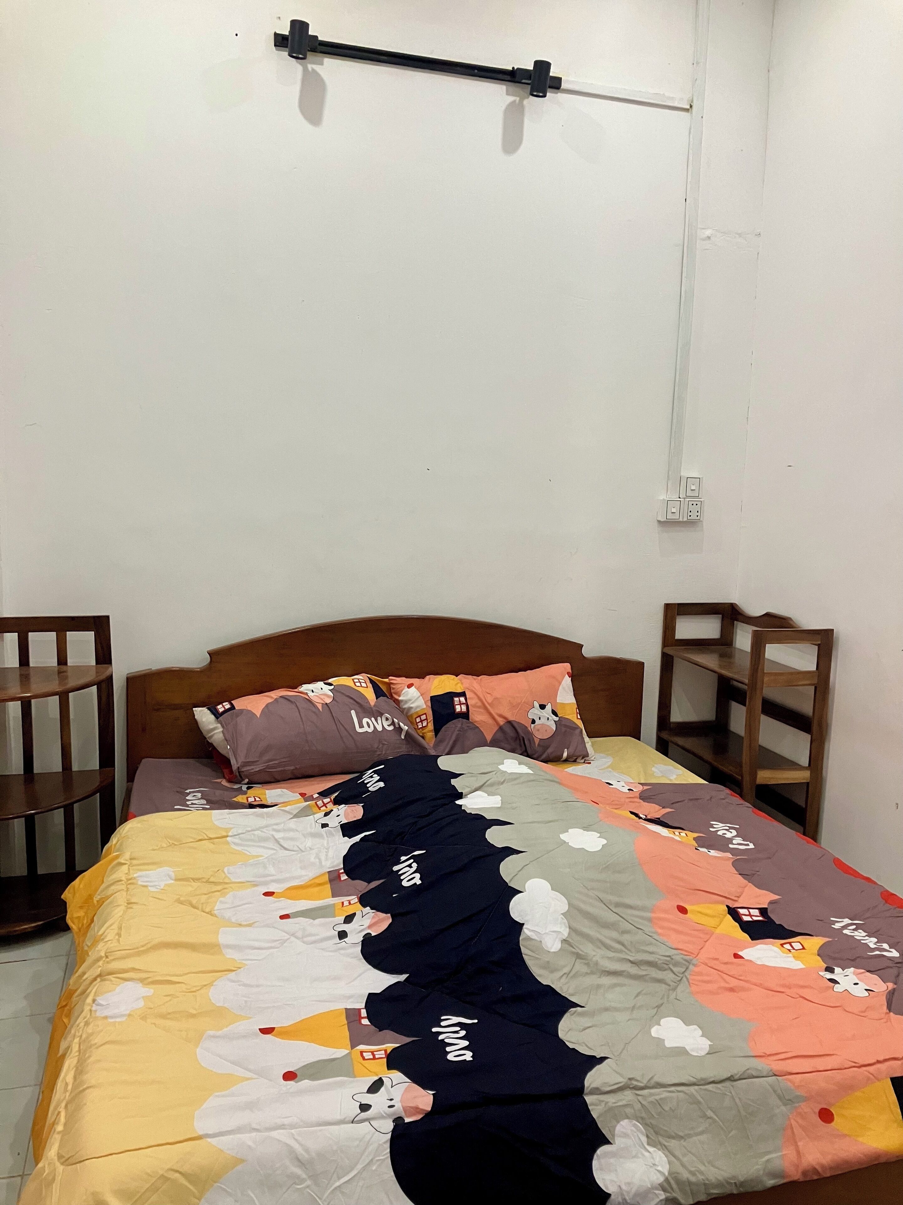 Un lit simple avec une couverture colorée, une tête de lit en bois et deux tables de chevet.